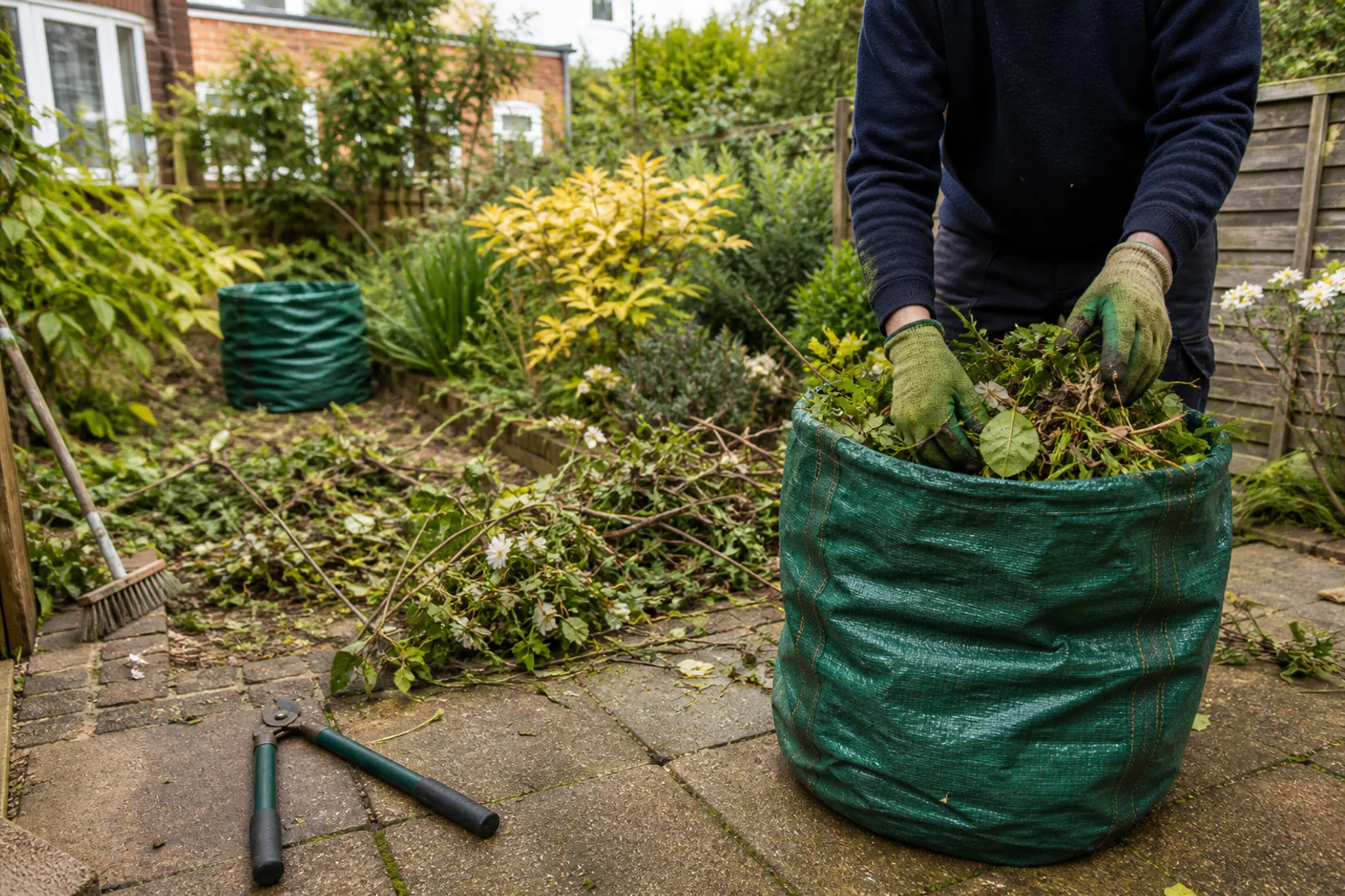 Gardener gathering cut garden material into a reusable green-waste sack
